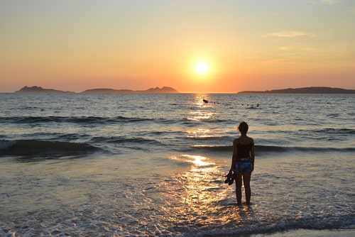 女性が海で夕陽を眺めている画像